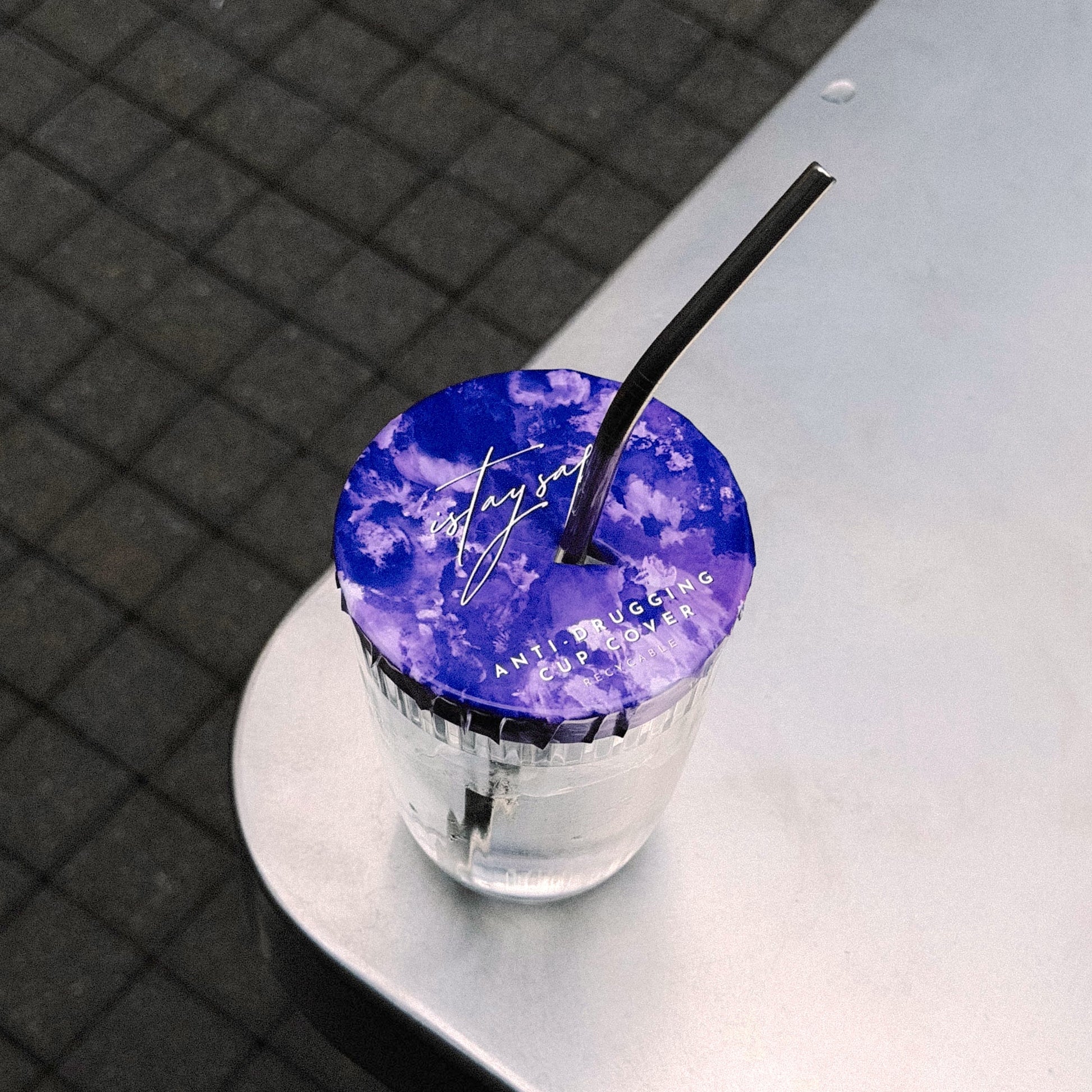 Clear glass with purple ISTAYSAFE cup cover and straw on a reflective surface